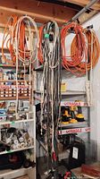Wide view of multiple extension cords of various colors hanging on peg near shelving units in basement.
