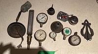 Overview of vintage gauges, bell, light socket, and other metal items on flat surface