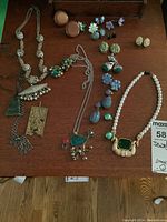 Photo showing assorted costume jewellery including necklaces and various clip-on earrings arranged on a wooden surface.