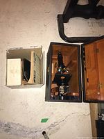 Top view showing the microscope inside its wooden carrying case and the accessory box next to it on concrete floor.