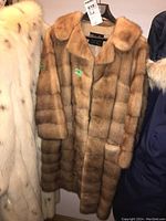 Full view of the mink fur coat hanging with other coats, showing natural light brown color and collar.