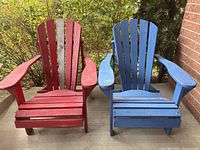 Two wooden Muskoka chairs side-by-side outdoors, one red and one blue, showing weathered paint and outdoor use.