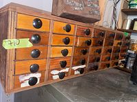 Side view of wooden organizer showing 35 drawers with black knob pulls, some paint chipping and numbers written on drawers