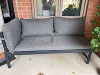 Front view of outdoor cushioned metal sofa with back and arm cushions in gray fabric upholstery.