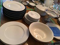 Lot with stacked white dinner plates, black chargers, white salad and side plates, and white ironstone bowls. Also visible Rosenthal Studio Linie mark on plate bottom.