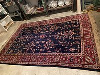Full view of the unrolled wool area rug showing the floral and geometric oriental design with dark blue center and red border.