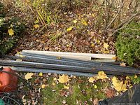 Several metal corner strips and beige downspout sections laid on ground covered with autumn leaves.