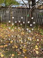 Three-panel metal garden screen standing outdoors among fallen leaves. Shows arched tops and multiple glass candle holders attached to each panel.