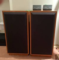 Front view of two large Studio-Lab floor speakers with black fabric grilles mounted, wood cabinet finish.