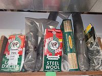 Photo of partial boxes and bags of Bull Dog steel wool rolls and Supreme industrial steel wool pads, showing packaging detail and quantity.