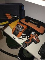 Photo showing Ridgid cordless drill, charger, drill bits, chisels, and tool pouch on table.