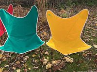 Frontal view of yellow and green butterfly chairs side by side on grass strewn with leaves