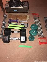 Photo showing various dumbbells including 15 lbs, 7 lbs labeled ALEX, 5 lbs grey hex dumbbells, and 5 lbs purple dumbbell along with chest expander and hand grippers.
