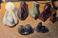 Photo showing 7 small bird figurines made from various wood, stone, and other materials on a wooden surface.
