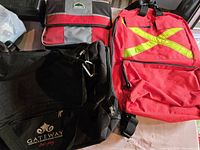 Photo showing large black duffel bag with Gateway logo, foldable gray and red freezer lunch bag, and red emergency backpack with reflective straps visible on front.