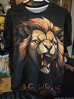 Front view of black T-shirt showing fierce lion face graphic and 'B.C. LIONS' text on front.