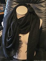 Black cashmere scarf displayed on dress form, showing wide soft fabric and fringed edges.