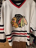 White Chicago Blackhawks jersey hanging, full front view showing embroidered logo and striping detail.
