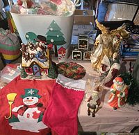 Photo showing the full set of Christmas decorations including ceramic house, angels, stocking, tree skirt, Santa figurines, pot holder, and small artificial Christmas tree