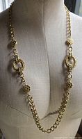 Front view of the chunky gold tone necklace on mannequin showing large chain links and ornate textured decorative links.