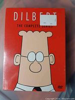 Front cover of sealed Dilbert Complete Series DVD set showing cartoon Dilbert character on red background.