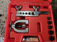 Double flaring tool kit opened showing metal clamp with multiple hole sizes and yoke tool in red plastic case.