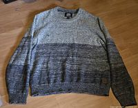 Front view of large knit sweater in various grey tones laid flat on wooden floor