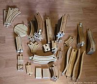 Wooden toy train track pieces laid flat on wooden floor, showing various track sections including curved tracks, straight tracks, and switches.