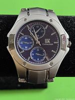 Close-up of LK Collection men's wristwatch, silver metal case and bracelet, blue dial with subdials and screw accents on bezel.