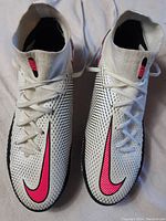 Top-down view of both white Nike Phantom soccer shoes with black dots and bright pink swoosh logos, showing the elastic sock ankle collars and laces.