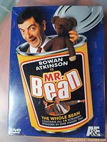 Front cover of the sealed DVD set with Rowan Atkinson as Mr. Bean holding a teddy bear, showing the tin packaging shaped like a bean can.