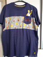 Front view of navy blue t-shirt with grey Duff Beer print stripe and chest pocket with Homer Simpson graphic