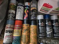 Front view of assorted spray paint cans arranged closely, showing brand labels and colors.