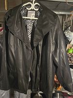 Front view of black leather coat hanging on a hanger, shows wide collar and smooth leather exterior.