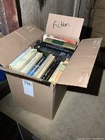 Photo of open cardboard box labeled 'Fiction' filled with fiction novels.