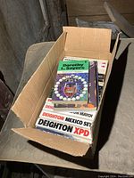 Photo showing a cardboard box filled with softcover books, on a mattress.