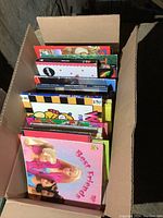 Top view of box filled with children's softcover and hardcover books showing colorful covers and titles.