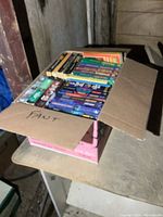 Top-down view of a cardboard box filled with paperback novels, showing spines of various books.