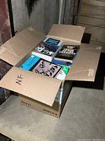Box of mixed books with various titles visible on the covers and spines inside an open cardboard box.