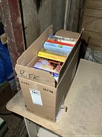 View of a closed cardboard box filled with novels seen from above, showing spine titles and authors
