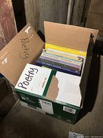 Open cardboard box labeled 'Poetry' filled with various poetry books standing upright.