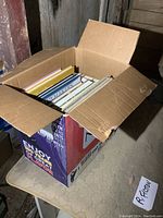Photo of a cardboard box filled with various books, viewed from above showing a mix of sizes and colors.