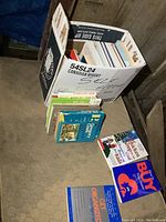 Cardboard box filled with assorted books including cookbooks and children's literature.