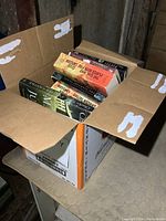 Open cardboard box showing multiple paperback novels stacked inside including visible titles by Stieg Larsson and others.
