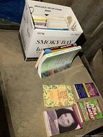 Photo showing a white box labeled Smoky Bay full of books, some books lying outside the box on a mattress.