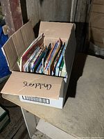 Box filled with children's books, viewed from above showing many books standing vertically.