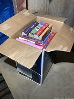 Top view of a shipping box filled with paperback novels, showing a variety of colorful spines and titles.