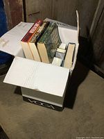 Box open showing several novels inside, visible spines and covers including John Grisham, Dean Koontz, James Patterson.