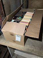 Cardboard box of novels, showing various book titles and colorful spines.