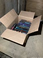 Cardboard box containing a stack of novels arranged lying flat, shot from an angle showing box and contents well.